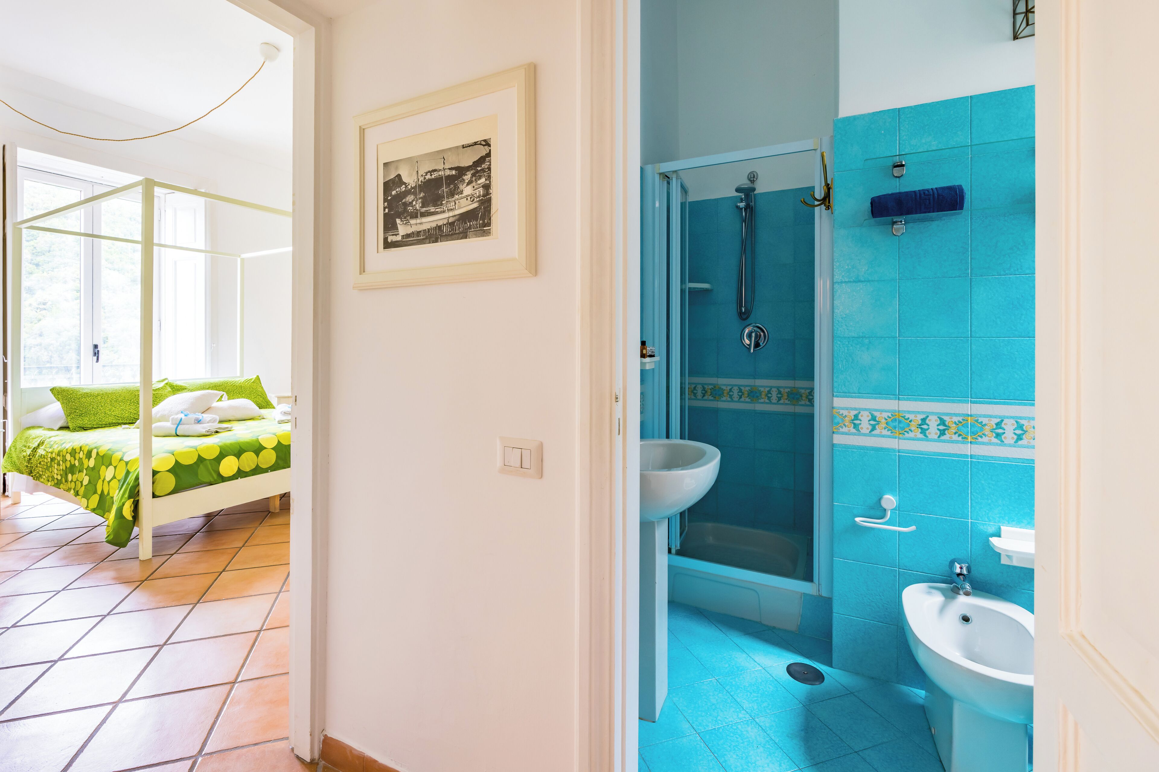 Een kamer met een bed, een lijst met een afbeelding en een badkamer met douche en wastafel.