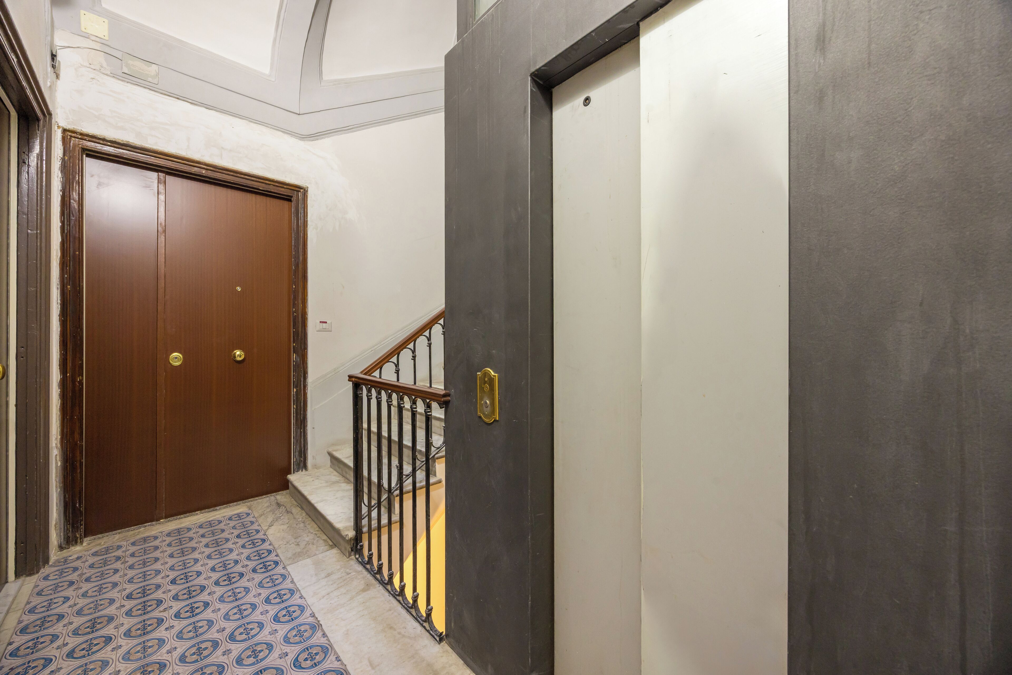 A hallway with a wooden door, a metal gate, and a patterned floor.