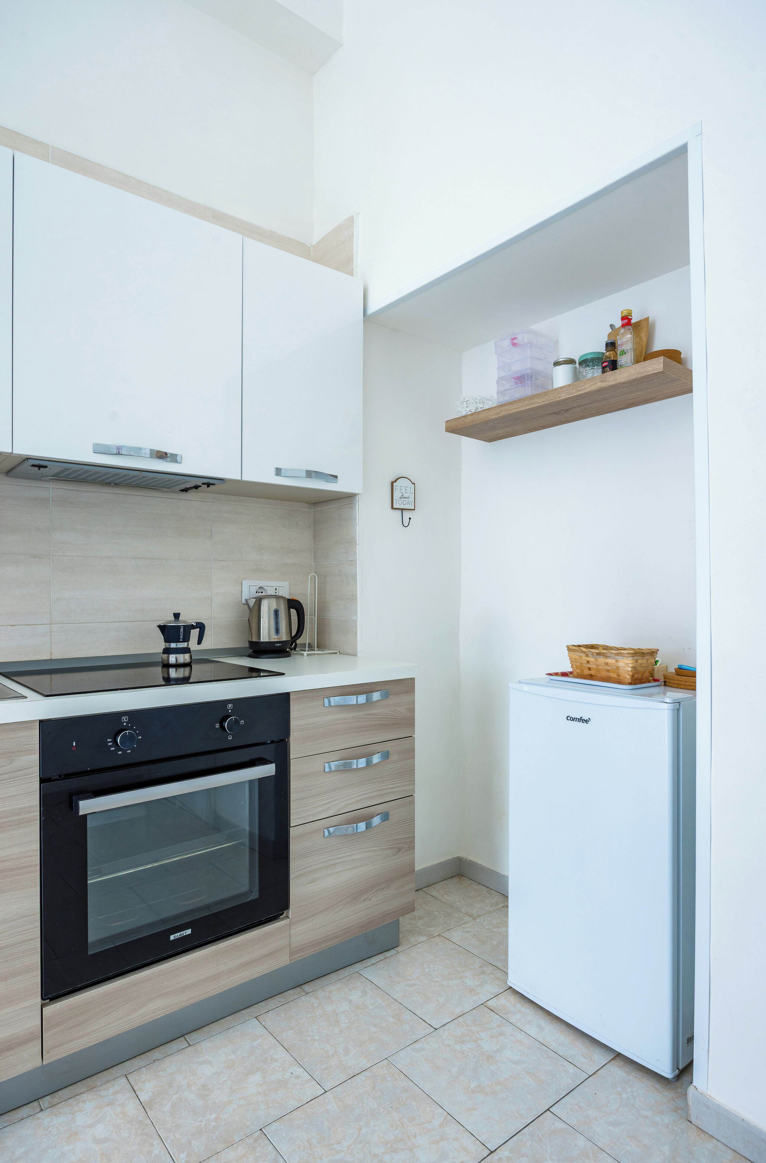 A modern kitchen with a built-in oven, a coffee maker, and a white refrigerator.