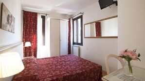 A bedroom with a bed, a desk with a lamp, a mirror, and a TV mounted on the wall. - albergo ai Tolentini (Venice)
