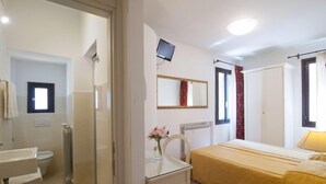 A hotel room with a bed, bedside table, chair, and a small desk with a chair. There is a window with curtains, a radiator, and a television mounted on the wall. - albergo ai Tolentini (Venice)
