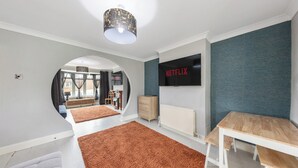 A modern living room with a large TV, a wooden table, and a cozy fireplace. - 4 Bd House - Sleeps 8 With Garden & Parking (Gillingham)