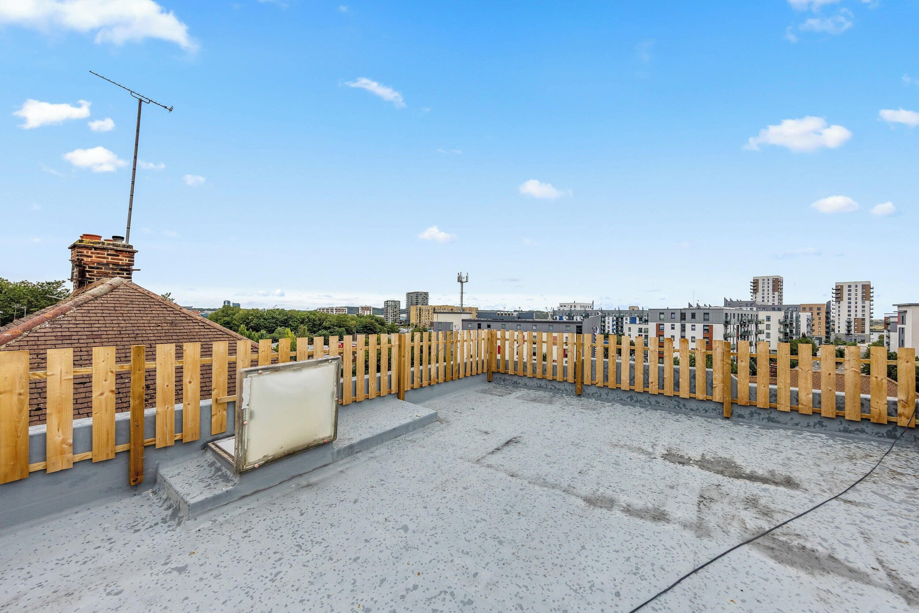 Una terraza en la azotea con un cerco de madera, una chimenea y vistas a edificios de la ciudad.