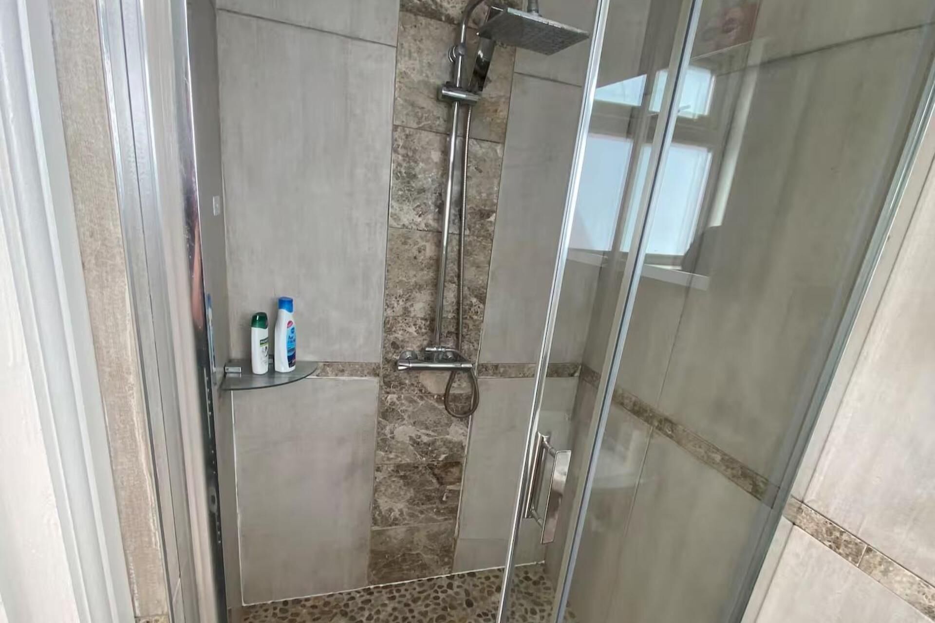 Ein Duschbereich mit Glasabtrennung, einer Steinwand und Ablage für Pflegeprodukte.