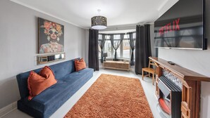 A modern living room with a blue sofa, a large TV, and a fireplace. - 4 Bd House - Sleeps 8 With Garden & Parking (Gillingham)