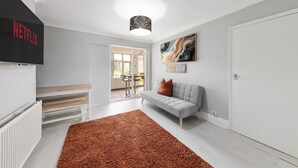 A modern living room with a grey sofa, a brown rug, a flat-screen TV, and a ceiling light. - 4 Bd House - Sleeps 8 With Garden & Parking (Gillingham)