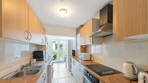 A modern kitchen with wooden cabinets, stainless steel appliances, and a black induction cooktop. - 4 Bd House - Sleeps 8 With Garden & Parking (Gillingham)