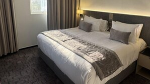 Ein modernes Hotelzimmer mit einem großen Bett, grauen Vorhängen und einem Fenster mit Ausblick.