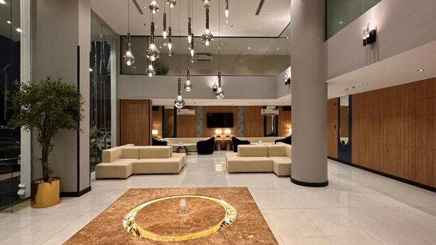 Eine moderne Lobby mit einer zentralen Sitzgruppe, einem großen runden Teppich und hängenden Pendelleuchten.
