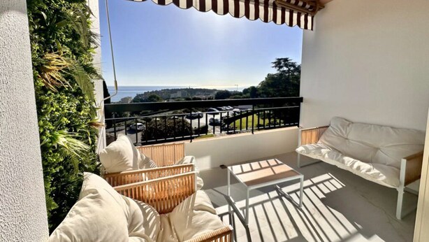 A balcony with wicker furniture, a white sofa, and a view of the cityscape.