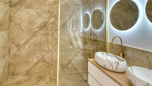 A bathroom with marble walls, a modern sink, and a glass-enclosed shower.