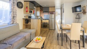 A compact living space with a kitchenette, a sofa, a dining table with chairs, and a fruit bowl. - Bora-Bora Mobile Home 289 with Shared Pool, Private Terrace and Garden (Les mathes)