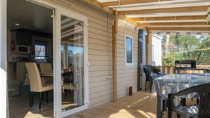 An open patio with a table and chairs, a grill, and a sliding glass door leading to an interior space with a kitchen. - Bora-Bora Mobile Home 289 with Shared Pool, Private Terrace and Garden (Les mathes)