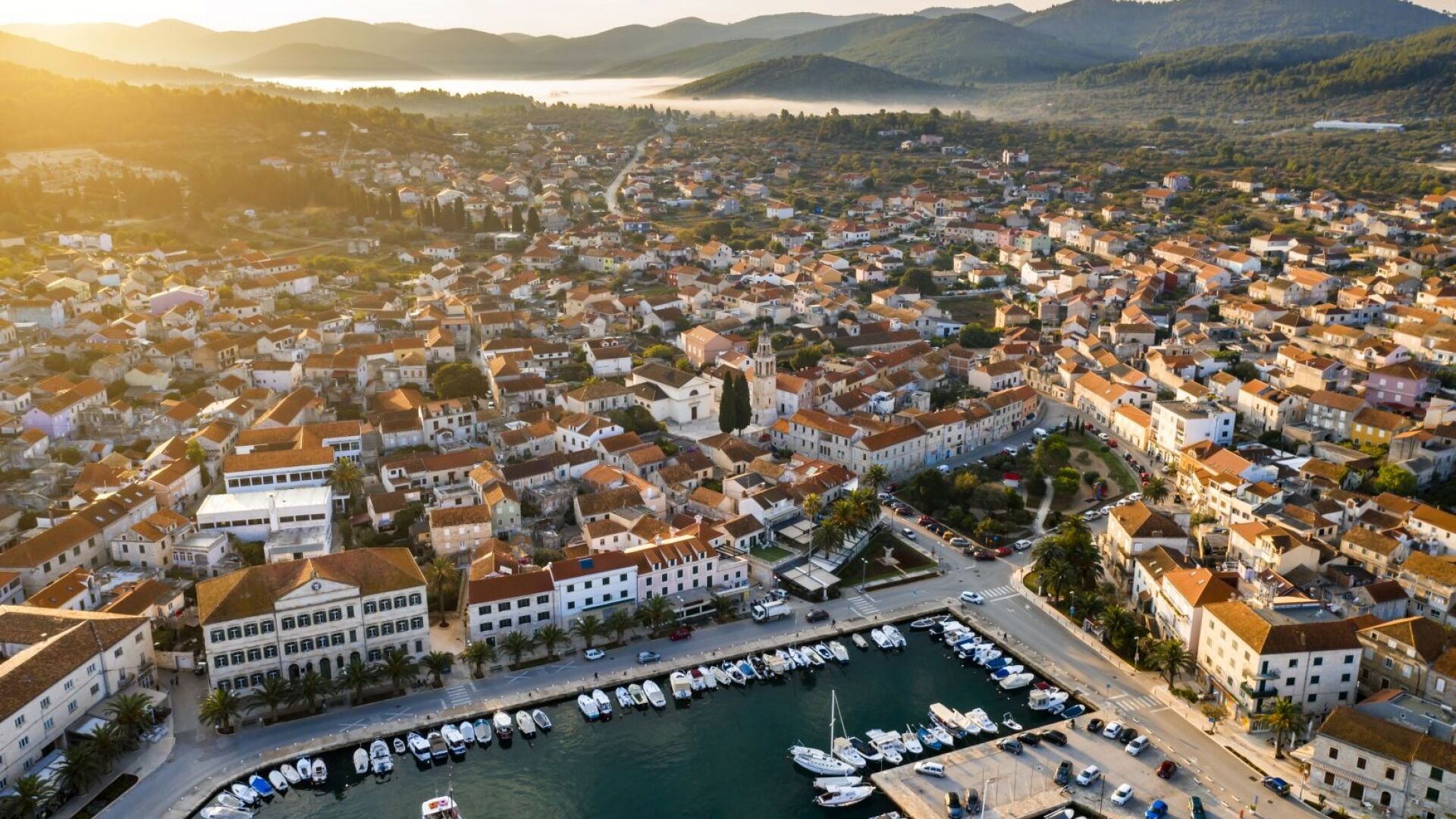An aerial view of a coastal town with a marina, dense housing, and a prominent church.