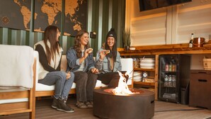 Three people sitting on a couch by a fire pit in a cozy room with a world map on the wall. - The Barn ~Minutes from Snoqualmie Casino! (Snoqualmie)