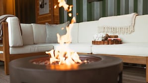 A modern living room with a white sofa, a round fire pit in the center, and a wooden side table with snacks. - The Barn ~Minutes from Snoqualmie Casino! (Snoqualmie)