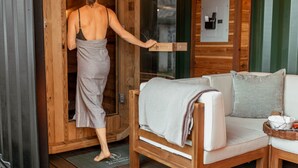 A wooden cabin interior with a wooden door, a white sofa with a blanket, and a small table with towels. - The Barn ~Minutes from Snoqualmie Casino! (Snoqualmie)