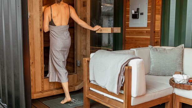 A wooden cabin interior with a wooden door, a white sofa with a blanket, and a small table with towels. - The Barn ~Minutes from Snoqualmie Casino! (Snoqualmie)