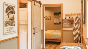 A compact room with a bed, a small table, and a door leading to another room.
