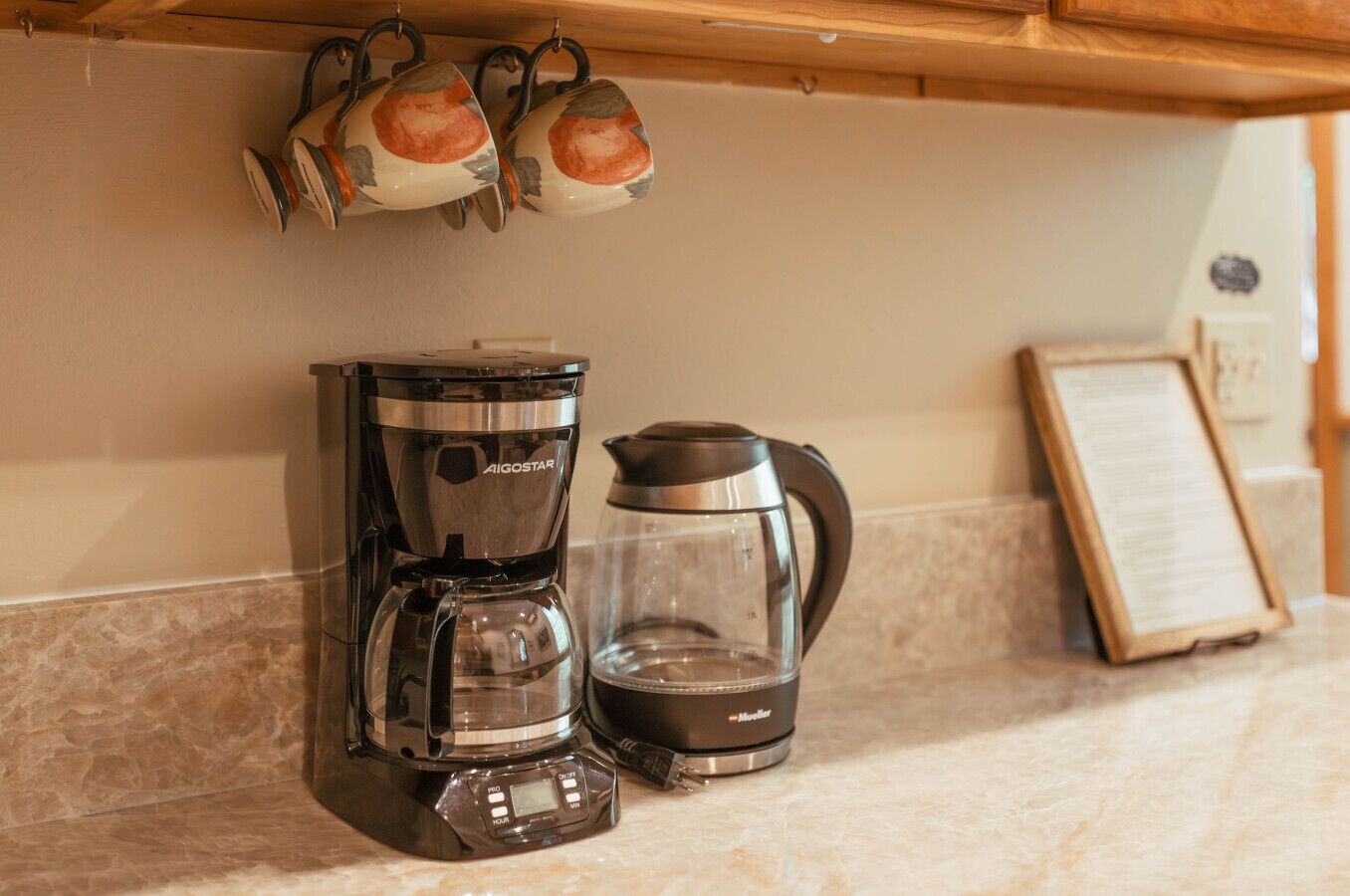 Un comptoir de cuisine avec une machine à café, une bouilloire et un menu encadré.