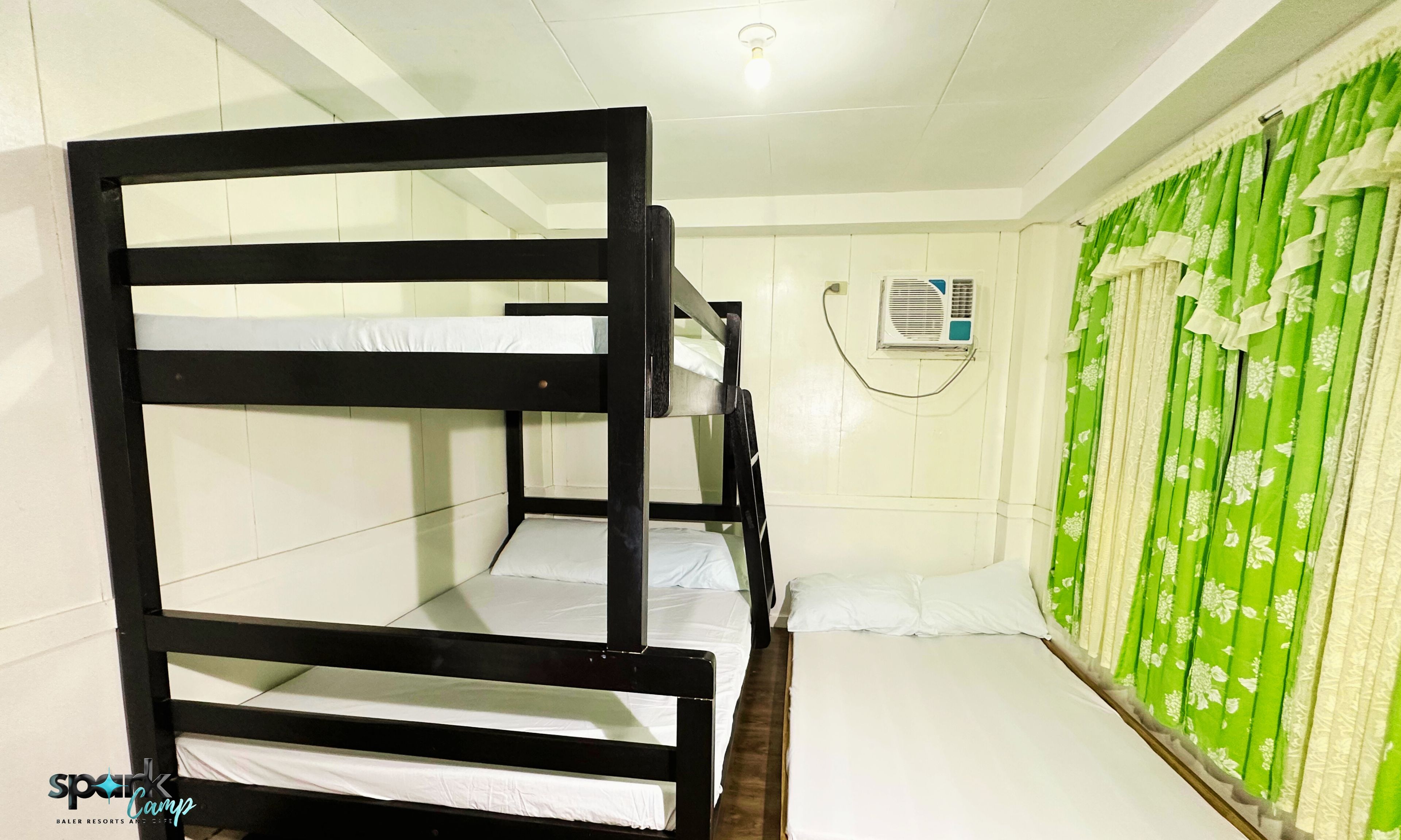 Une salle familiale avec des lits superposés, un rideau vert et un appareil de climatisation.