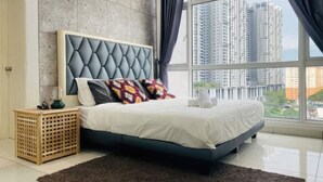 A modern bedroom with a tufted headboard, a large window with curtains, a wooden crate, and a dark rug. - Central Residence - Free Gym Pool (Kuala Lumpur)