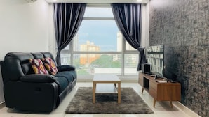 A modern living room with a black leather sofa, a wooden coffee table, and a dark rug. A wooden side table with a TV and remote control is against the wall. - Central Residence - Free Gym Pool (Kuala Lumpur)