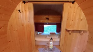 A cozy wooden cabin with a bunk bed, a small table with a bottle and glass, and a window with curtains. - TinyHouse "Cupid" by the lake, Mecklenburg Lake District (Fürstenberg/Havel)