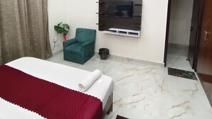 Un dormitorio moderno con cama, ventilador de techo, televisor montado en la pared y una silla verde.