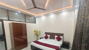 Habitación de hotel moderna con una cama grande, ventilador de techo, iluminación empotrada, un jarrón con girasoles y vista a la ciudad desde la ventana.