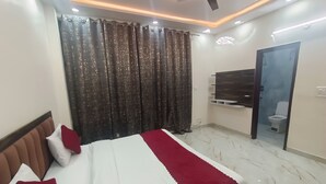 Un dormitorio moderno con cama, cortinas, ventilador de techo, televisor y baño visible a través de una puerta.