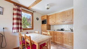 Une cuisine avec des meubles de rangement en bois, une table à manger avec des chaises, une fenêtre avec des rideaux et un luminaire au plafond.