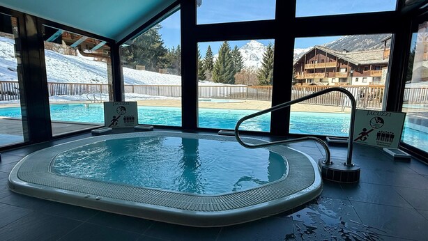 Une piscine intérieure avec vue sur les montagnes enneigées et un chalet.