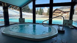 An indoor swimming pool with a view of snowy mountains and a chalet.