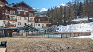 Un hôtel à plusieurs étages doté de balcons, d’une piscine et offrant une vue sur des montagnes enneigées.