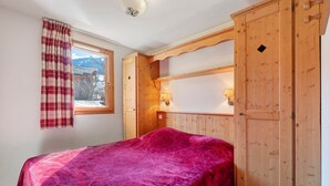 Une chambre à coucher avec un lit, une armoire en bois, une fenêtre avec des rideaux et une lampe.