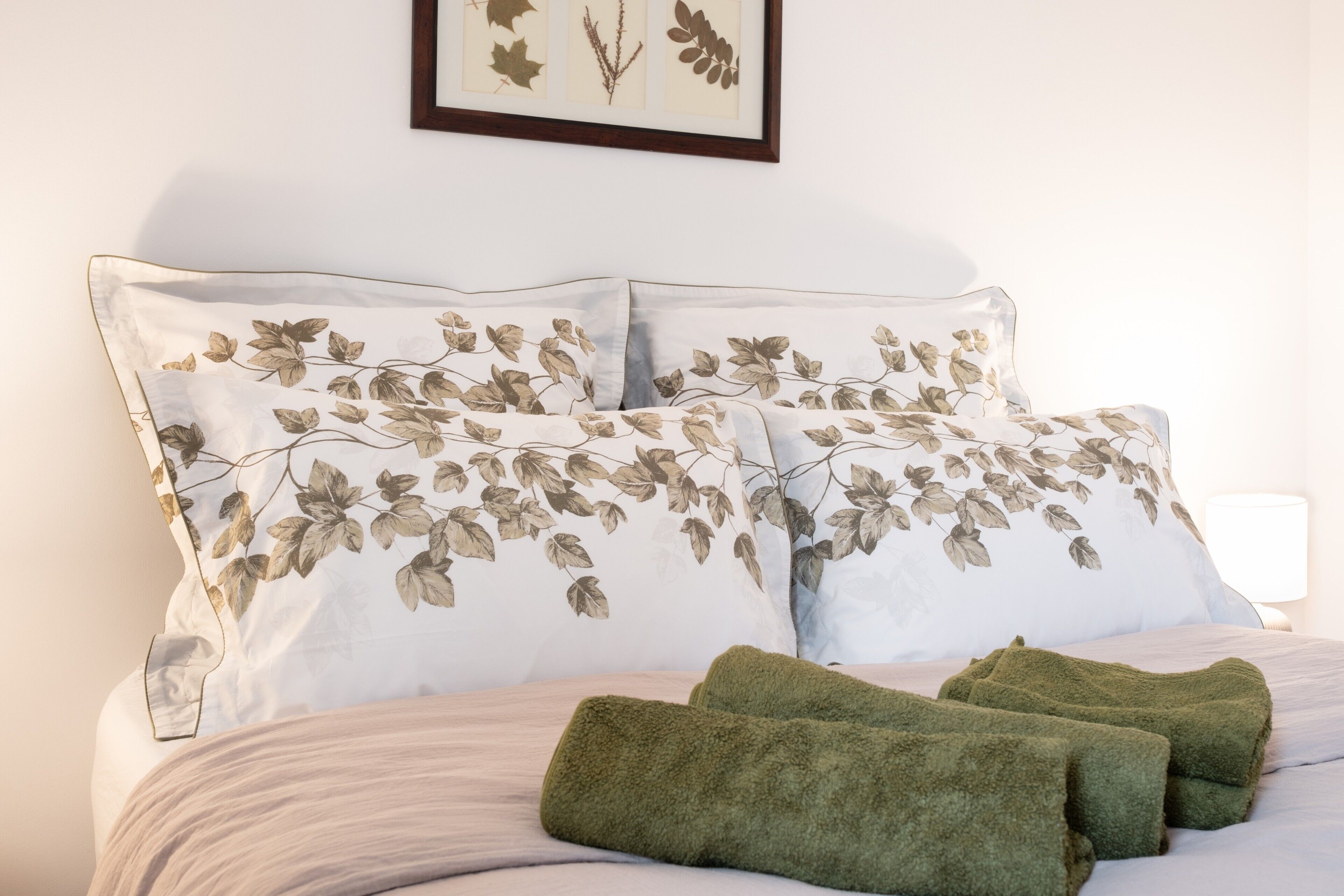 A neatly made bed with floral-patterned pillows and green towels.