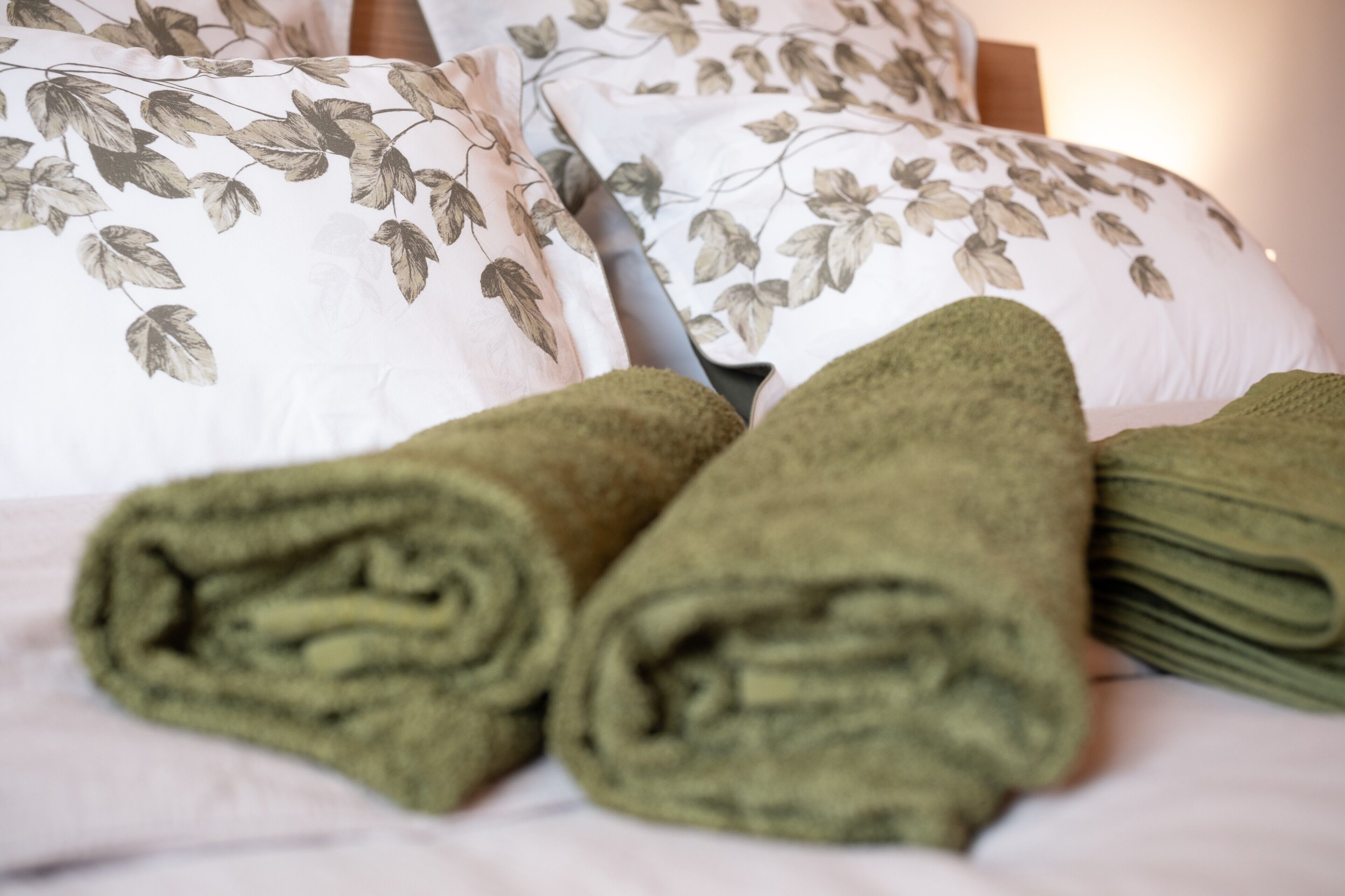 A bed with rolled green towels, a floral-patterned pillow, and a wooden headboard.