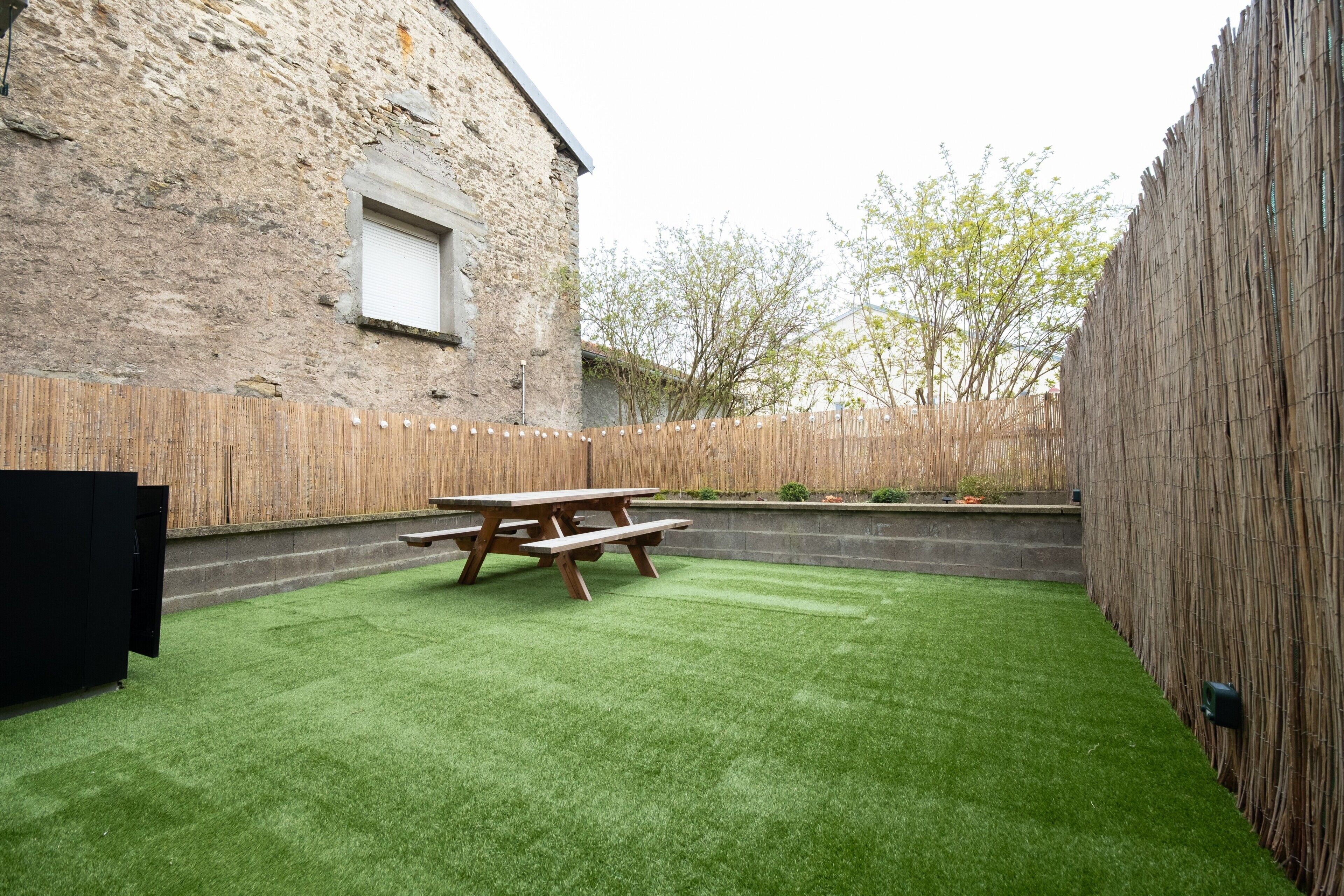 A backyard with artificial grass, a wooden picnic table, and a stone wall.