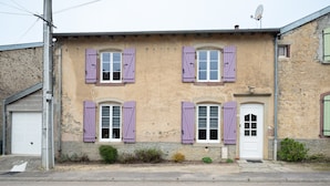Ein zweistöckiges Gebäude mit einer Steinfassade, violetten Fensterläden und einer weißen Tür.