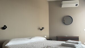 Un lit bien fait, avec des serviettes pliées, une table de chevet, une commode et un climatiseur fixé au mur.