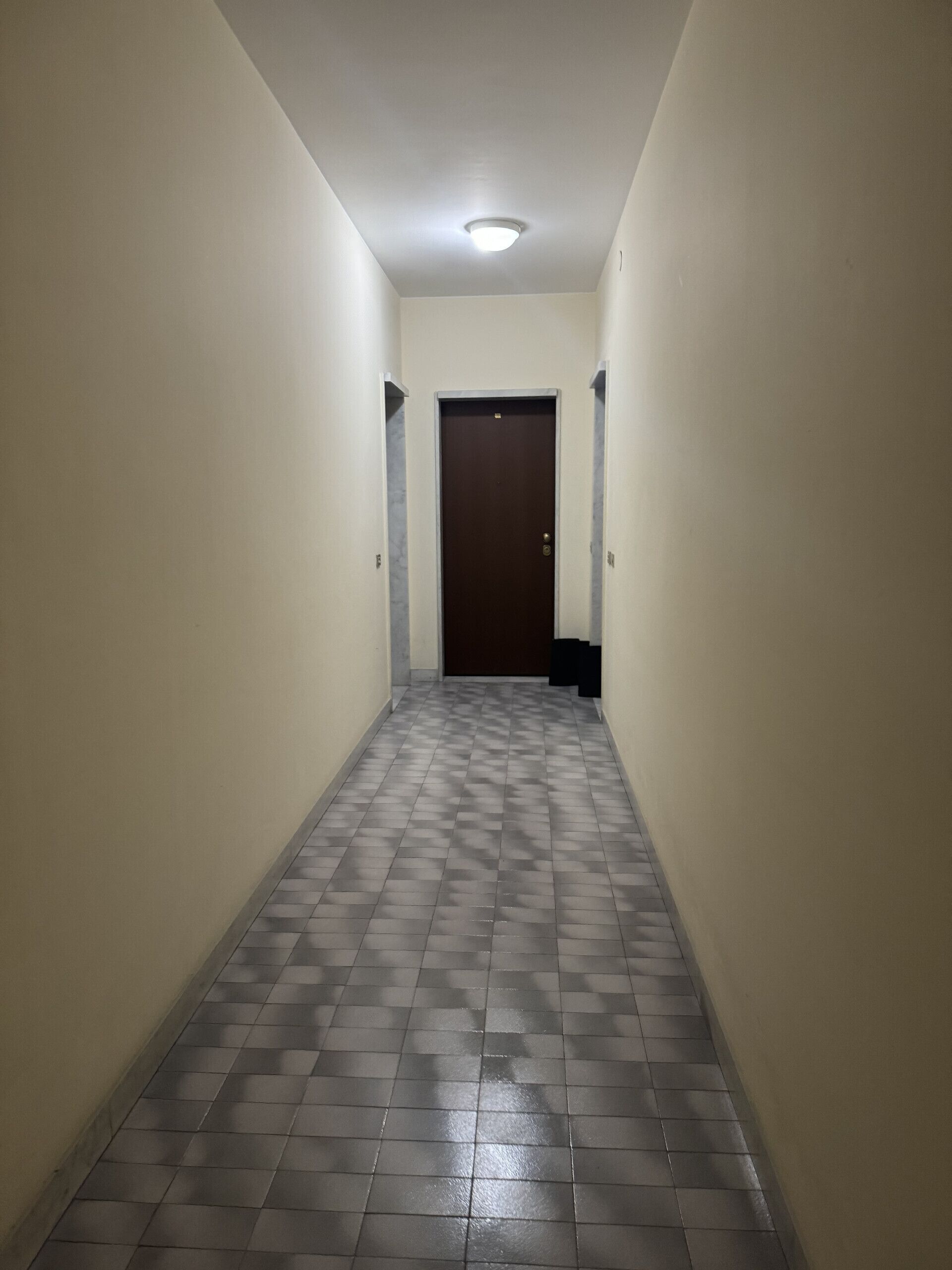 A narrow hallway with a tiled floor and a door at the end.