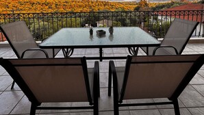 Een balkon met een glazen tafel en stoelen, met uitzicht op een landschap met herfstkleuren en heuvels in de verte.