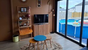 Un salón moderno con un televisor grande, estanterías de madera, una mesita y vistas a una piscina exterior.