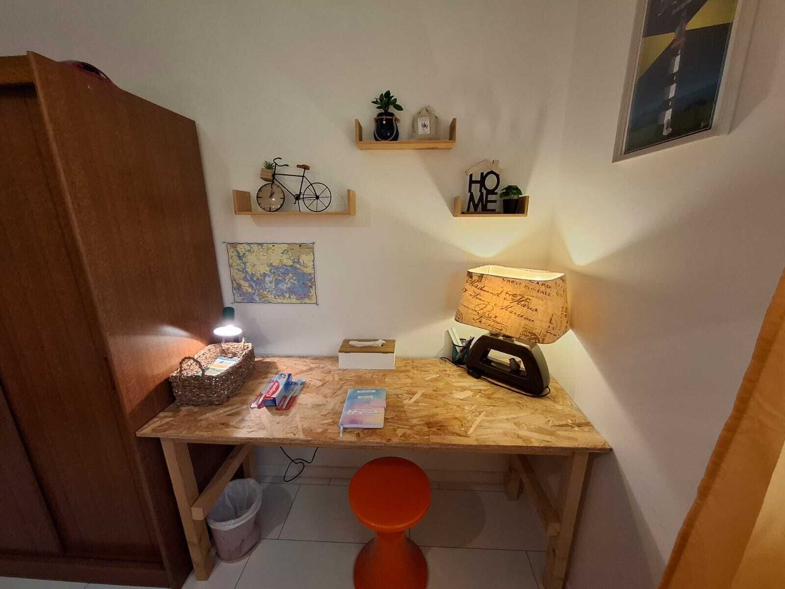 Een compacte werkruimte met een houten bureau, een lamp, een mand en een kaart aan de muur.