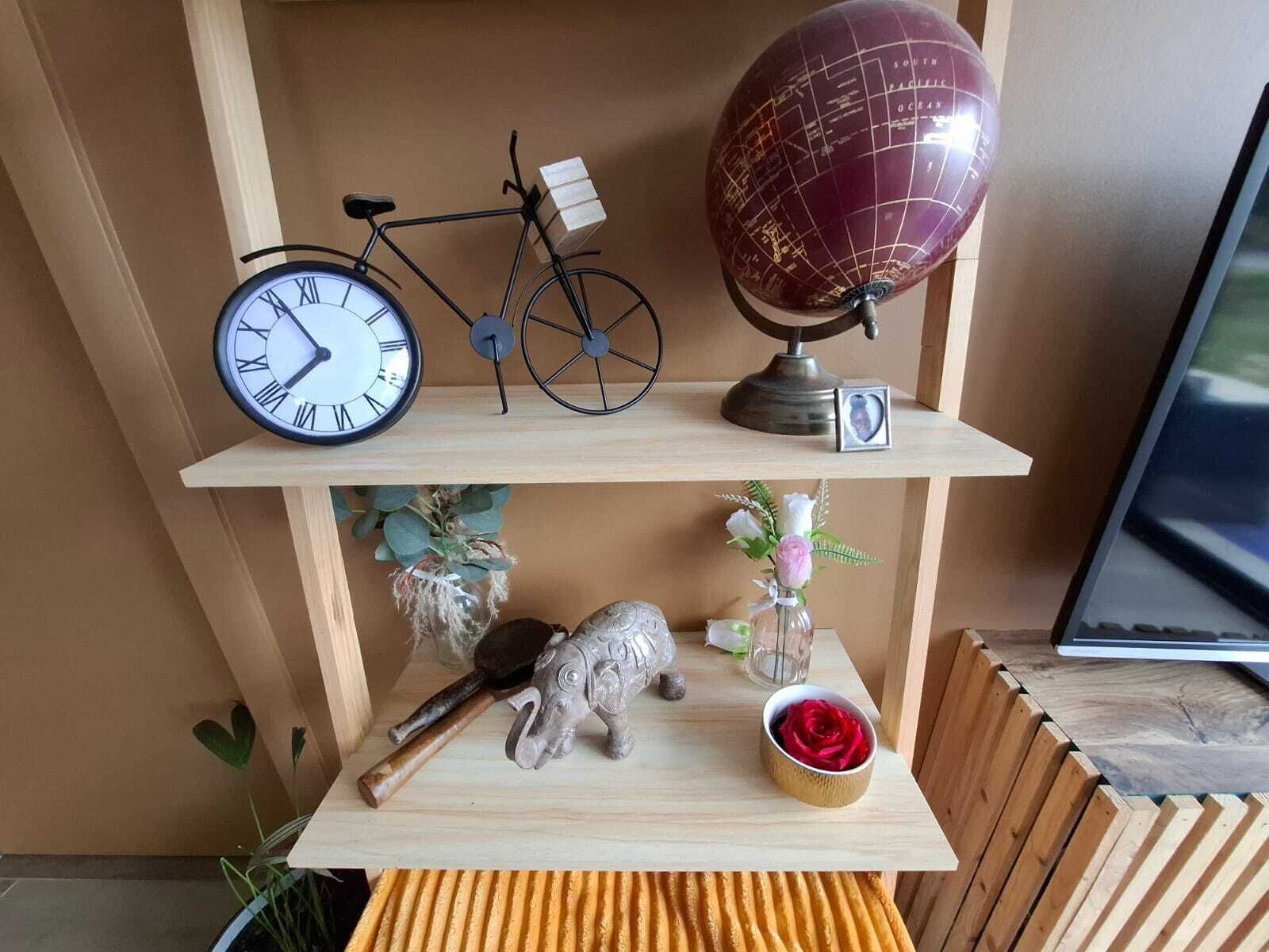 Une étagère en bois ornée d’une horloge, d’un globe terrestre et d’objets décoratifs, notamment une petite figurine d’éléphant et un vase rempli de fleurs.