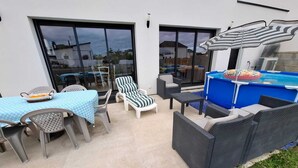 Un patio al aire libre con una mesa, sillas, sillones de descanso, una piscina pequeña y una sombrilla.