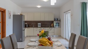 A modern kitchen with a dining area, equipped with a refrigerator, microwave, oven, and a dining table set for four. - Villa Ruža - Omiš by Villas Guide (Blato na Cetini)