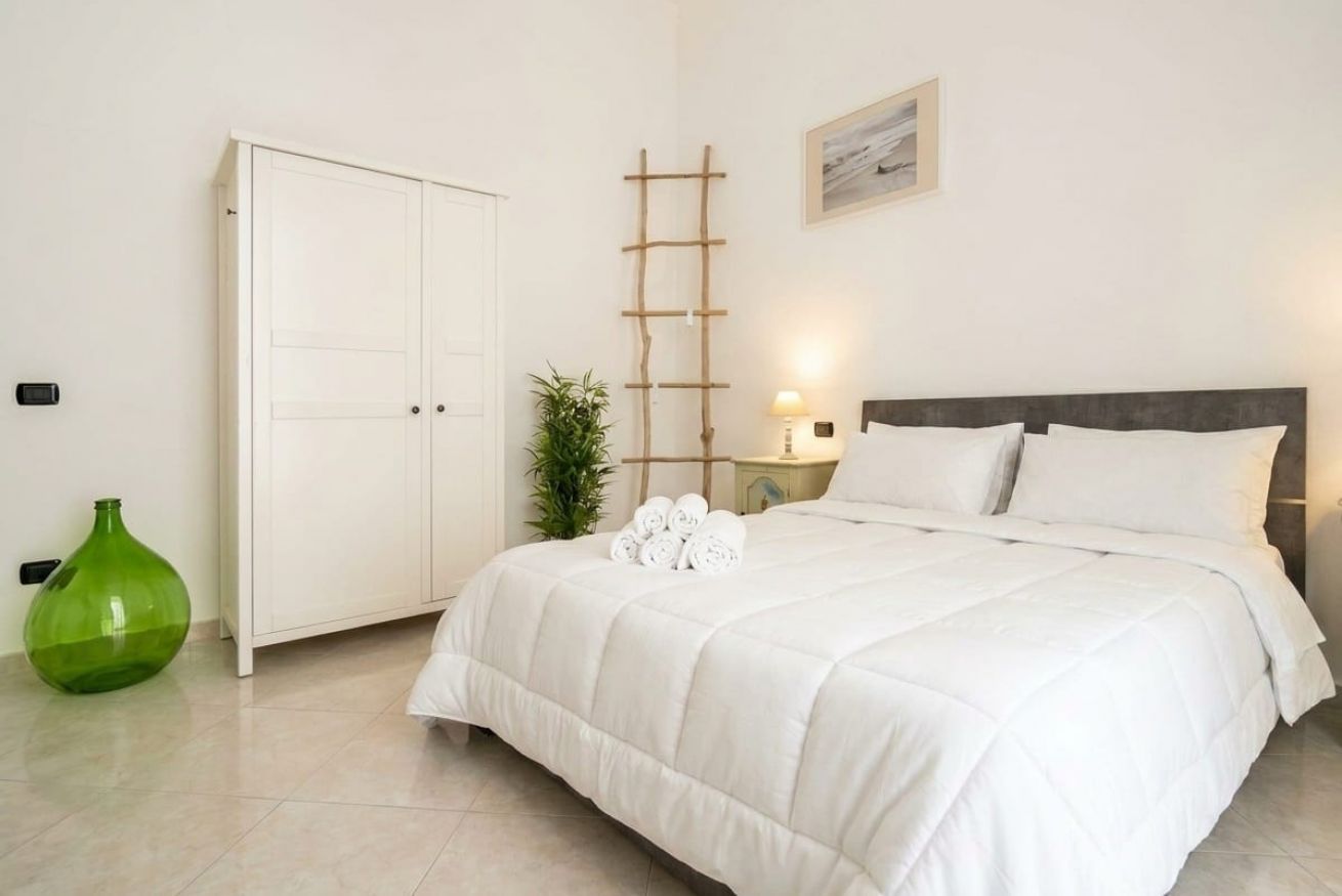 A bedroom with a bed, a wardrobe, a bedside table with a lamp, and a green vase.