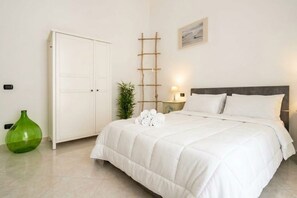 Een slaapkamer met een bed, een kledingkast, een nachtkastje met een lamp en een groene vaas.